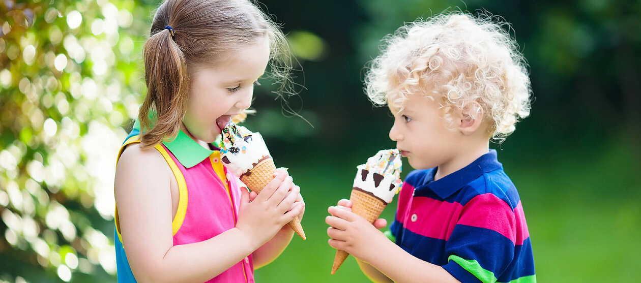 schöner Sommeranfang Kinder Junge und Mädchen essen Eis im sonnigen Garten 